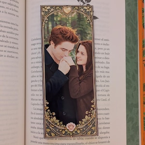 Puede incluir: Un marcapáginas con una imagen romántica de una pareja, enmarcada con un borde dorado ornamentado. La pareja está en un tierno abrazo, con una rosa en la parte inferior. El marcapáginas está colocado dentro de las páginas de un libro.