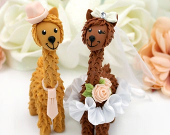 May include: A brown and tan llama wedding cake topper with the bride wearing a white veil and a pink flower on her head. The groom is wearing a pink hat and a pink tie.