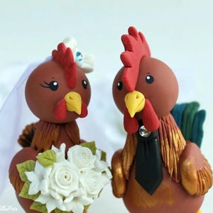 May include: A pair of rooster wedding cake toppers. The bride rooster is wearing a white veil and holding a bouquet of white roses. The groom rooster is wearing a black bow tie. Both roosters are brown with red combs and wattles.