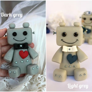Pu&ograve; includere: Due figurine di robot, una grigio scuro e l'altra grigio chiaro, con papillon bianco e nero e cuori. I robot hanno un viso sorridente e si tengono per mano.