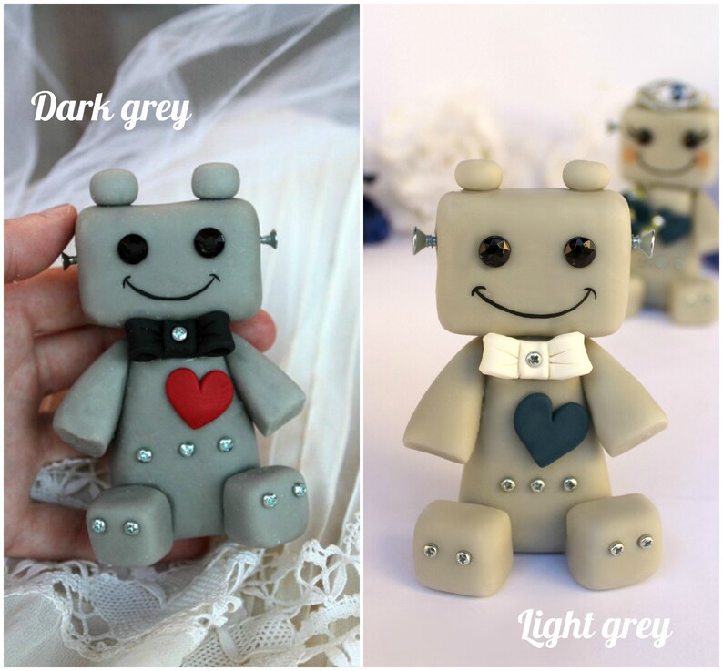 Pu&ograve; includere: Due figurine di robot, una grigio scuro e l'altra grigio chiaro, con papillon bianco e nero e cuori. I robot hanno un viso sorridente e si tengono per mano.