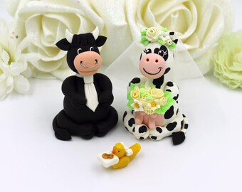 Op de afbeelding: Een bruidstaarttopper van een zwarte stier en een witte koe met zwarte vlekken. De stier draagt een zwart pak en een witte stropdas. De koe draagt een witte sluier en houdt een boeket gele en witte bloemen vast.