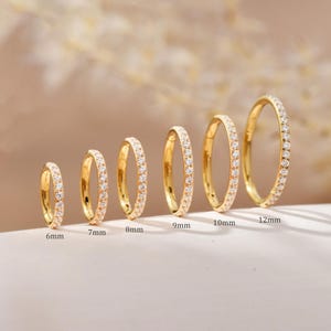 Könnte beinhalten: Eine Sammlung von sechs goldfarbenen Creolen, jede mit kleinen, klaren Edelsteinen besetzt. Die Ohrringe variieren in der Größe von 6 mm bis 12 mm Durchmesser. Die Ohrringe werden auf einer hellen Oberfläche präsentiert.