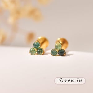 Könnte beinhalten: Ein Paar goldfarbene Schraub-Ohrstecker, die jeweils mit drei kleinen, runden, gesprenkelten grünen Moosachat-Steinen in einer dreieckigen Anordnung besetzt sind. Die Ohrstecker haben einen flachen, runden Verschluss und ein poliertes Metall-Finish.