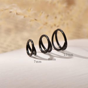 Könnte beinhalten: Drei schwarze, kreisförmige Creolen in einer Reihe, die ein zweilagiges Design aufweisen. Die Ringe sind mit ihren jeweiligen Durchmessern von 7 mm, 8 mm und 10 mm beschriftet, was die spezifische Größe für jedes Schmuckstück angibt.