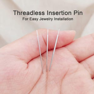 Peut inclure: Trois broches d'insertion sans filetage en métal argenté pour l'installation de bijoux. Le texte en haut indique Threadless Insertion Pin For Easy Jewelry Installation. Ces outils fins et droits présentent une pointe effilée à une extrémité.