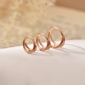 Peut inclure: Trois créoles de couleur or rose disposées en rangée, chacune présentant une finition lisse et polie ainsi qu'un design à segment articulé. Les anneaux varient légèrement en taille, le plus grand étant à droite et le plus petit à gauche.