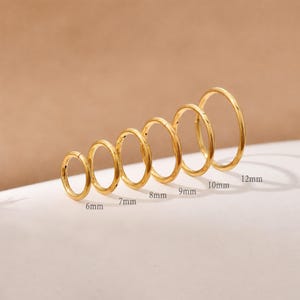May include: A set of six gold-coloured circular hoop rings arranged in a row from smallest to largest. Each ring is labelled with its diameter in millimetres, ranging from 6mm, 7mm, 8mm, 9mm, 10mm, to 12mm, indicating the specific size of each individual hoop.