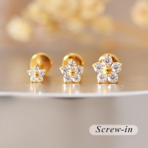 May include: Three gold-tone stud earrings in a flower shape, each featuring five clear round stones surrounding a central gold bead. The earrings have a screw-in backing mechanism. The text "Screw-in" is visible in the bottom right corner.