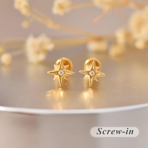 Könnte beinhalten: Ein Paar goldfarbene Ohrstecker mit einem vierzackigen Sternendesign und einem kleinen klaren Stein in der Mitte jedes Sterns. Die Ohrringe verfügen über einen Schraubverschluss, wie durch den Text Screw-in unten rechts angegeben.