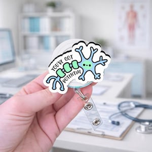 May include: A white and blue badge reel with a cartoon neuron design. The badge reel has the text "YOU'VE GOT POTENTIAL" in black and green. The reel has a clear plastic strap and a metal clip.