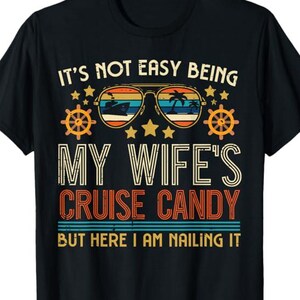 May include: Black t-shirt with a retro design. The graphic includes sunglasses with a cruise ship and palm trees, along with the text "IT'S NOT EASY BEING MY WIFE'S CRUISE CANDY BUT HERE I AM NAILING IT."