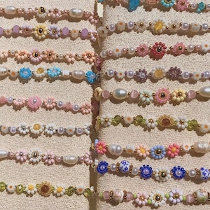 Pode incluir: Uma coleção de colares de contas com detalhes florais e pérolas. Os colares apresentam várias cores, incluindo rosa, azul, amarelo e branco. As contas são dispostas em padrões florais e intercaladas com pérolas.