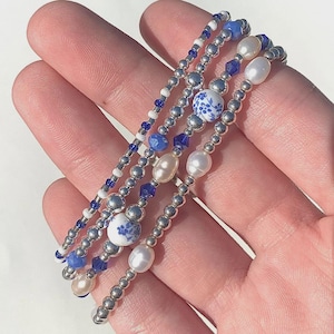 Puede incluir: Un conjunto de cuatro pulseras de cuentas. Las pulseras presentan cuentas plateadas, cuentas blancas y azules, cristales azules y perlas blancas. Algunas pulseras tienen cuentas de porcelana con diseños florales azules.