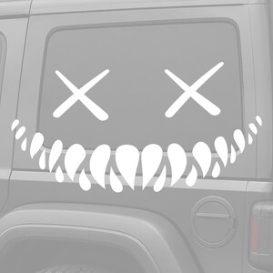 May include: White vinyl decal featuring a stylized face with crossed-out eyes and a toothy grin. The decal is designed to be applied to a vehicle's window, adding a unique and edgy aesthetic. The design is simple yet striking.
