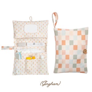 Pode incluir: Um trocador e uma bolsa a condizer. O trocador é creme com traços verticais em laranja, amarelo e verde. A bolsa tem um padrão xadrez em pêssego, verde e creme. O trocador tem vários bolsos e um dispensador de lenços.