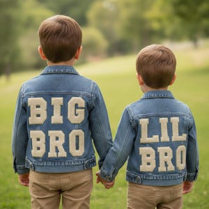 May include: Two children wearing matching denim jackets with the words "BIG BRO" and "LIL BRO" appliqued on the back. The jackets are a medium wash blue with tan lettering. The children are holding hands.