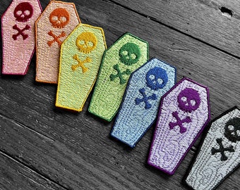 May include: Eight embroidered coffin patches in a rainbow of colors. Each patch features a skull and crossbones design.
