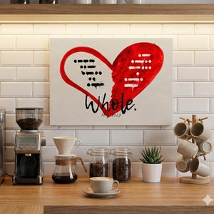 Könnte beinhalten: Eine Küchenszene mit einer Espressomaschine aus Edelstahl, einer Kaffeemühle und einem Kunstwerk mit einem roten Herzdesign und dem Wort "Whole". Eine Tasse Kaffee auf einer Untertasse und eine kleine Sukkulente in einem weißen Topf.