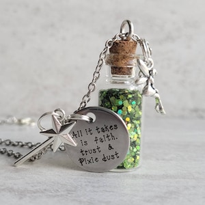 May include: A silver necklace with a small glass bottle filled with green glitter. The bottle has a cork stopper and is attached to a silver chain. The necklace also has a charm with the text "All it takes is faith, trust & pixie dust".