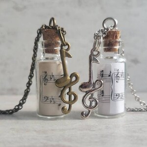 May include: Two silver necklaces with glass bottles filled with sheet music and a silver and bronze music note charm.