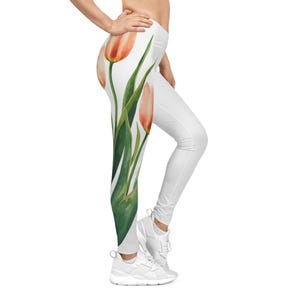 May include: White leggings with a watercolor design of orange and pink tulips with green leaves. The leggings are form-fitting and have a high waist. The floral pattern is on the left leg.