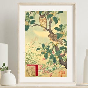 May include: Framed Japanese woodblock print featuring two owls perched on a tree branch with green leaves and yellow flowers. The artwork has a soft, muted color palette with a full moon in the background. A red and gold panel with Japanese text is in the lower left.
