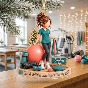 May include: A clear acrylic ornament featuring a cartoon figure in a teal scrub top and black leggings, surrounded by physical therapy equipment including a red exercise ball, foam roller, and resistance bands. Text reads: Sophia, Just A Girl Who Loves Physical Therapy.