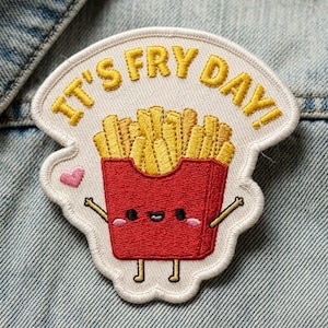 May include: Embroidered patch featuring a cartoon image of a red french fry container with a smiling face and arms, filled with golden fries. The patch has the text "IT'S FRY DAY!" in yellow, with a small pink heart.