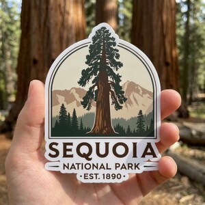 May include: A die-cut sticker featuring a central tall sequoia tree, a forest, and mountain peaks in a cream and green color palette. The text reads SEQUOIA NATIONAL PARK EST. 1890 in dark brown lettering at the bottom of the arched design.