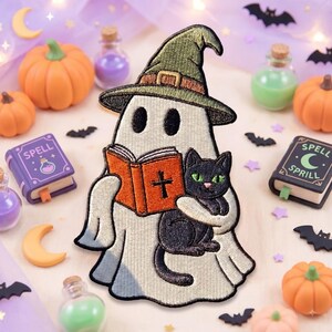 May include: An embroidered patch featuring a white ghost wearing a green witch hat, holding an orange book with a black cross on the cover, and embracing a black cat with green eyes. The patch has detailed stitching and a white border.