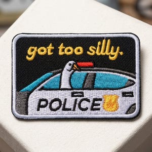 May include: Embroidered patch featuring a police car with a goose in the driver's seat. The patch has the words "got too silly" in yellow above the car and "POLICE" in white below. The car is white and blue.