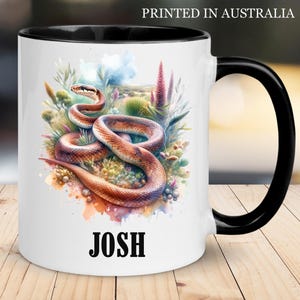 May include: White ceramic mug with a black handle and rim, featuring a watercolour illustration of a snake coiled among plants. The name "JOSH" is printed in bold black letters. Text at the top reads "PRINTED IN AUSTRALIA".