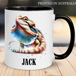 May include: White ceramic mug with a black handle and rim, featuring a colourful watercolour illustration of a bearded dragon. The lizard has blue, orange, and brown tones. The name "JACK" is printed in bold black letters. The text "PRINTED IN AUSTRALIA" is at the top.