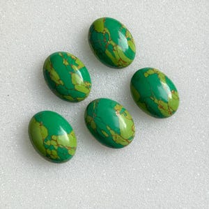 May include: Five oval-shaped gemstones with a vibrant green hue and intricate patterns of lighter green and gold veining. The polished stones are arranged on a white surface, showcasing their natural beauty and unique textures.