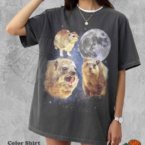 Op de afbeelding: Een antracietgrijs T-shirt met korte mouwen en een grafische print van drie quokka's en een volle maan tegen een sterrenhemel. Het shirt heeft een ronde hals en een relaxte pasvorm, met de tekst Color Shirt Pepper eronder gedrukt.