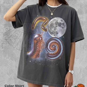 May include: A charcoal grey short-sleeve t-shirt featuring a graphic print of two brown millipedes and a full moon against a starry space background. The shirt has a crew neckline and a loose, relaxed fit, showcasing a detailed cosmic design.