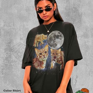 May include: Black t-shirt featuring a graphic of three cats, a full moon, and a starry background. The shirt has the text "Color Shirt Black" at the bottom left and a logo at the bottom right.