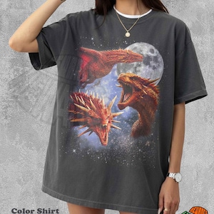 May include: A charcoal gray oversized t-shirt featuring a graphic print of three red dragons against a starry night sky with a full moon. The shirt has a crew neckline and short sleeves. The text Color Shirt Pepper is printed in the bottom left corner.