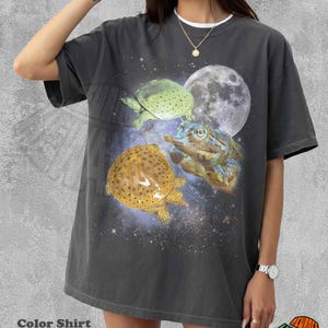 May include: Pepper-colored t-shirt featuring a celestial design with three turtles, a full moon, and a starry background. The shirt has a white collar and the text "Color Shirt Pepper" at the bottom.