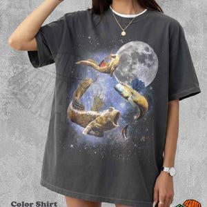 May include: Dark grey t-shirt with a graphic of three fish in a starry night sky with a full moon. The shirt has a white collar and the text "Color Shirt Pepper" at the bottom. The shirt is a relaxed fit.