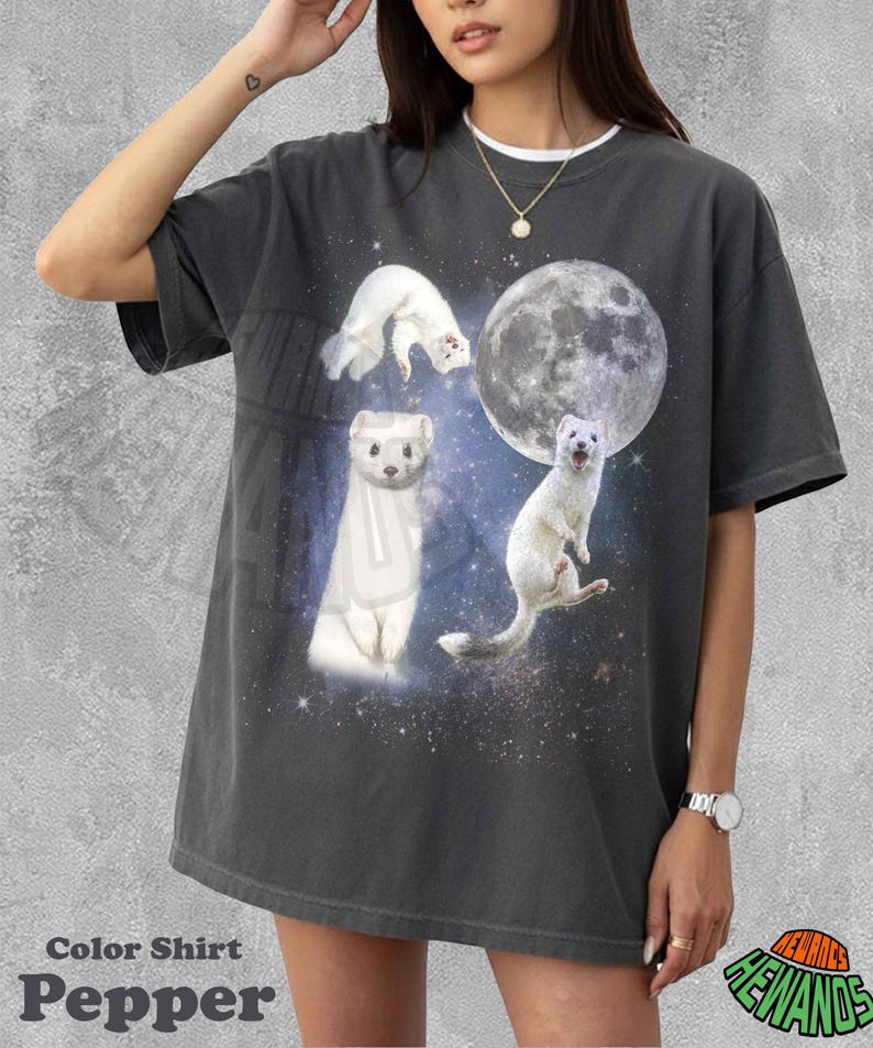 May include: Dark grey t-shirt featuring a whimsical design of white ferrets against a starry space background with a large moon. The shirt has a white collar and the text "Color Shirt Pepper".