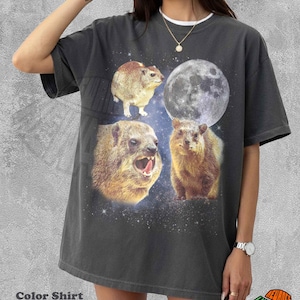 Puede incluir: Camiseta gris oscuro con un gráfico que presenta tres damanes y una luna llena sobre un fondo estrellado. La camiseta tiene un cuello blanco y el texto "Color Shirt Pepper".