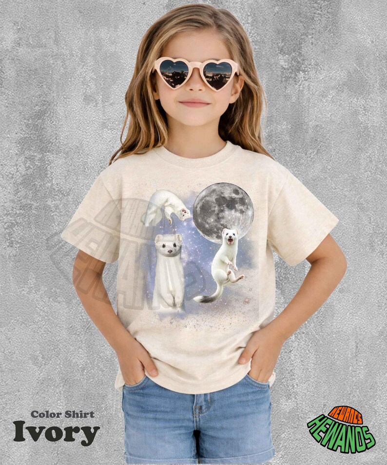 May include: Ivory-colored t-shirt featuring a whimsical design of white ferrets with a full moon. The shirt includes the text "Color Shirt" and "Ivory" at the bottom. The girl is wearing heart-shaped sunglasses and denim shorts.