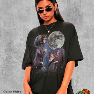 May include: Black graphic t-shirt featuring three Tasmanian devils with open mouths, a full moon, and a starry background. The shirt has the text "Color Shirt Black" at the bottom.