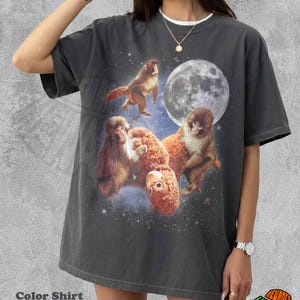 May include: Dark gray t-shirt featuring a whimsical design of monkeys in space with a full moon and stars. The shirt has a white collar and the text "Color Shirt Pepper".