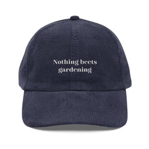Puede incluir: Gorra de béisbol de pana azul marino con el texto blanco "Nothing beets gardening". La gorra tiene una visera curva y una parte superior redondeada. Un sombrero informal para los entusiastas de la jardinería.