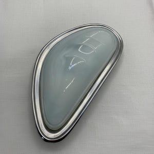 May include: A modern, oval-shaped ceiling light fixture. The light has a frosted glass shade with a curved design, set within a polished silver metal frame. The fixture is designed for indoor use.