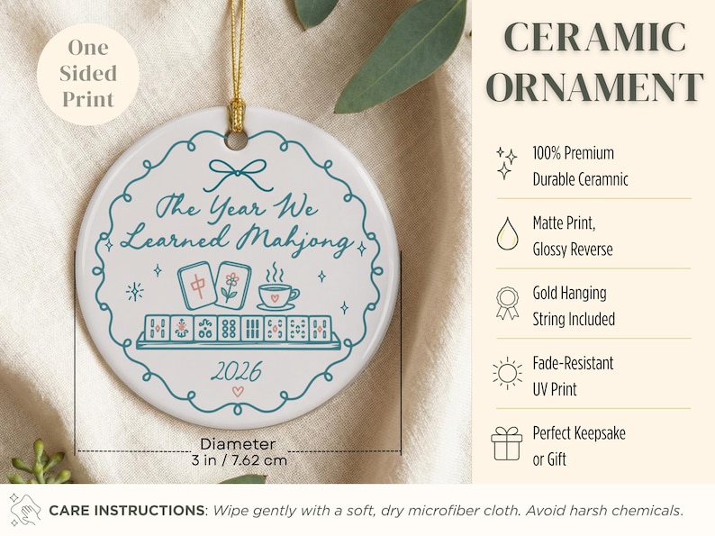 May include: A round white ceramic ornament with a 3-inch diameter, featuring a teal decorative border, a gold hanging string, and the text The Year We Learned Mahjong 2026. The design includes illustrations of mahjong tiles and a teacup.
