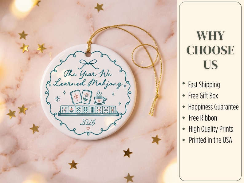 May include: A round white ceramic ornament with a gold hanging string. The design features a teal scalloped border, the text "The Year We Learned Mahjong", a graphic of mahjong tiles and a teacup, and the year "2026" with a small red heart.